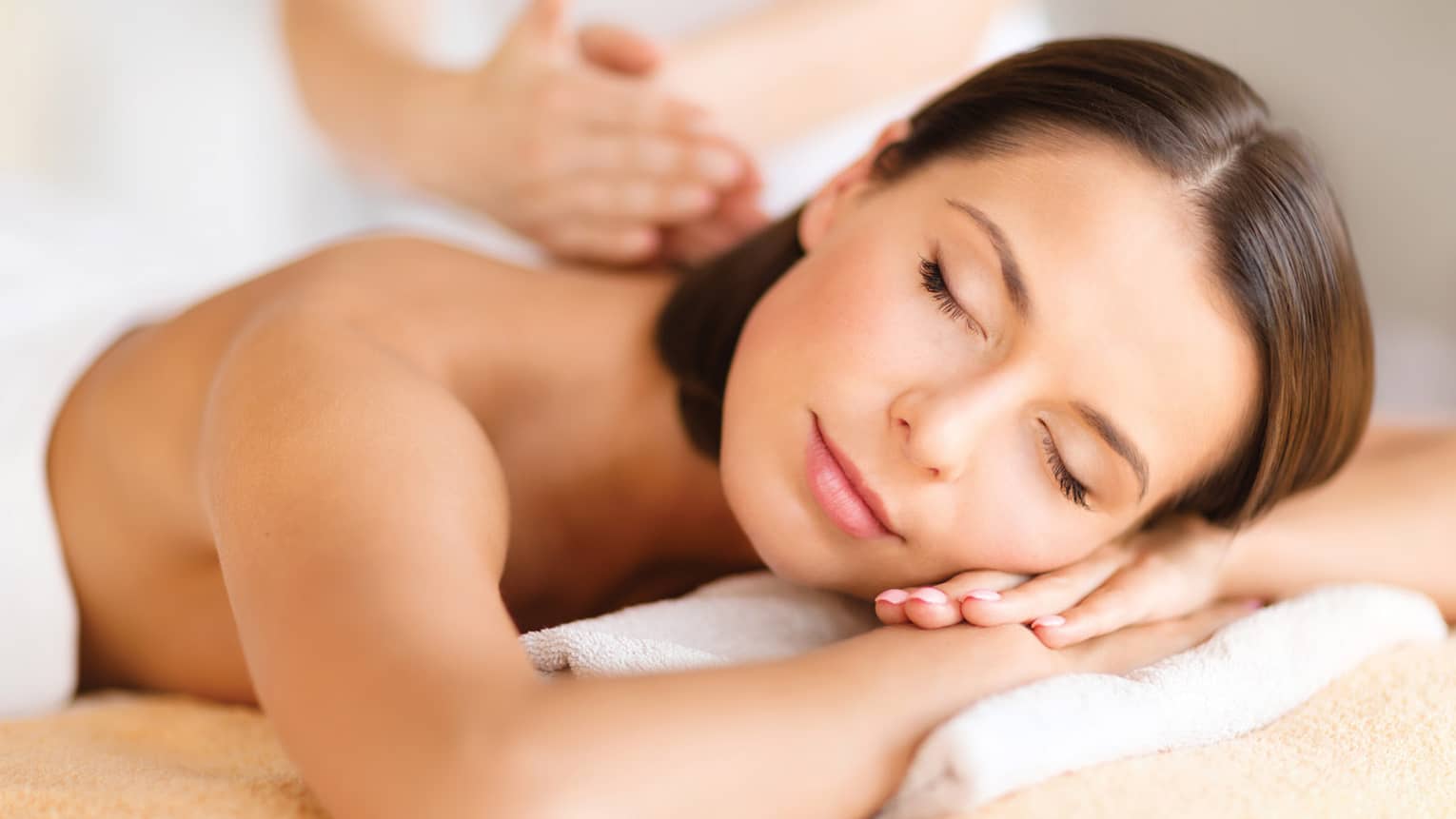 Woman lies on massage table, closes eyes. rests head on arms as spa staff massages back