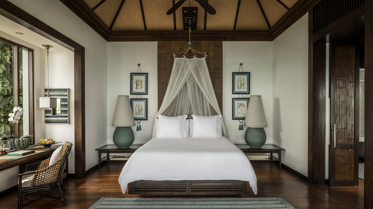 Family Pool Villa bed with white net canopy, large lamps on each side, wood floors, desk by window