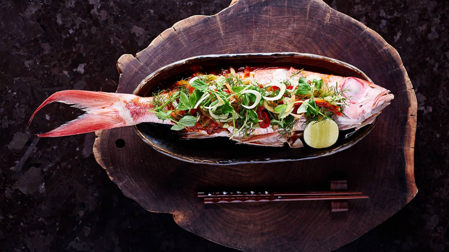 Whole grilled fish on skillet with fresh greens, vegetables, lime