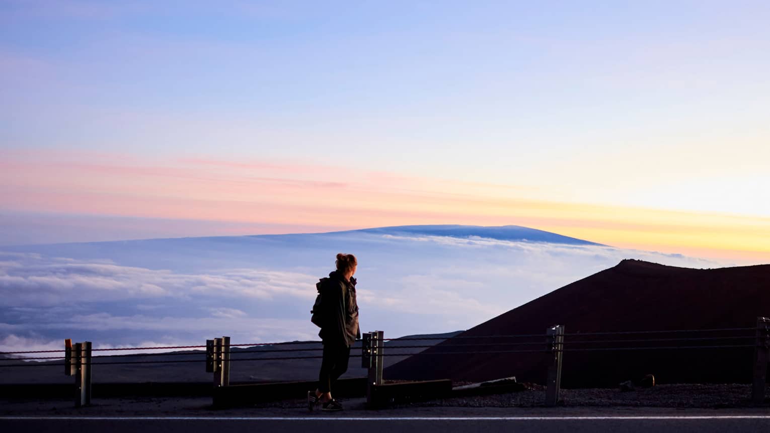 Silhouette of woman hiking, looking out over mountain, sky at sunset