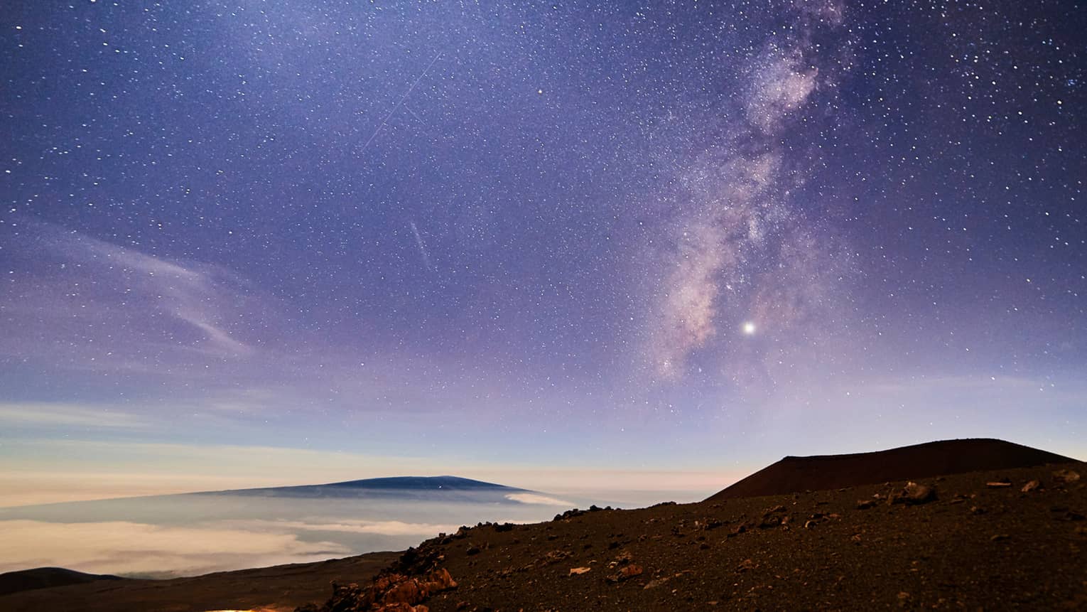Sunrise under starry sky above mountain, volcanic rocks
