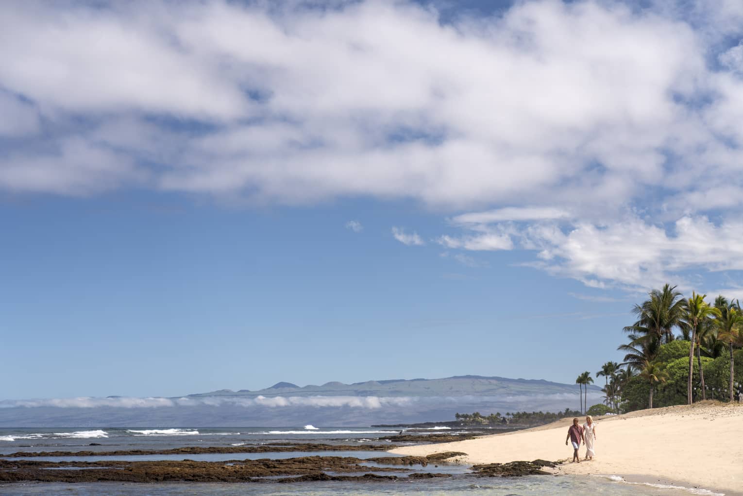 A couple walks along the beach in Hualalai near Four Seasons Resort Hualalai