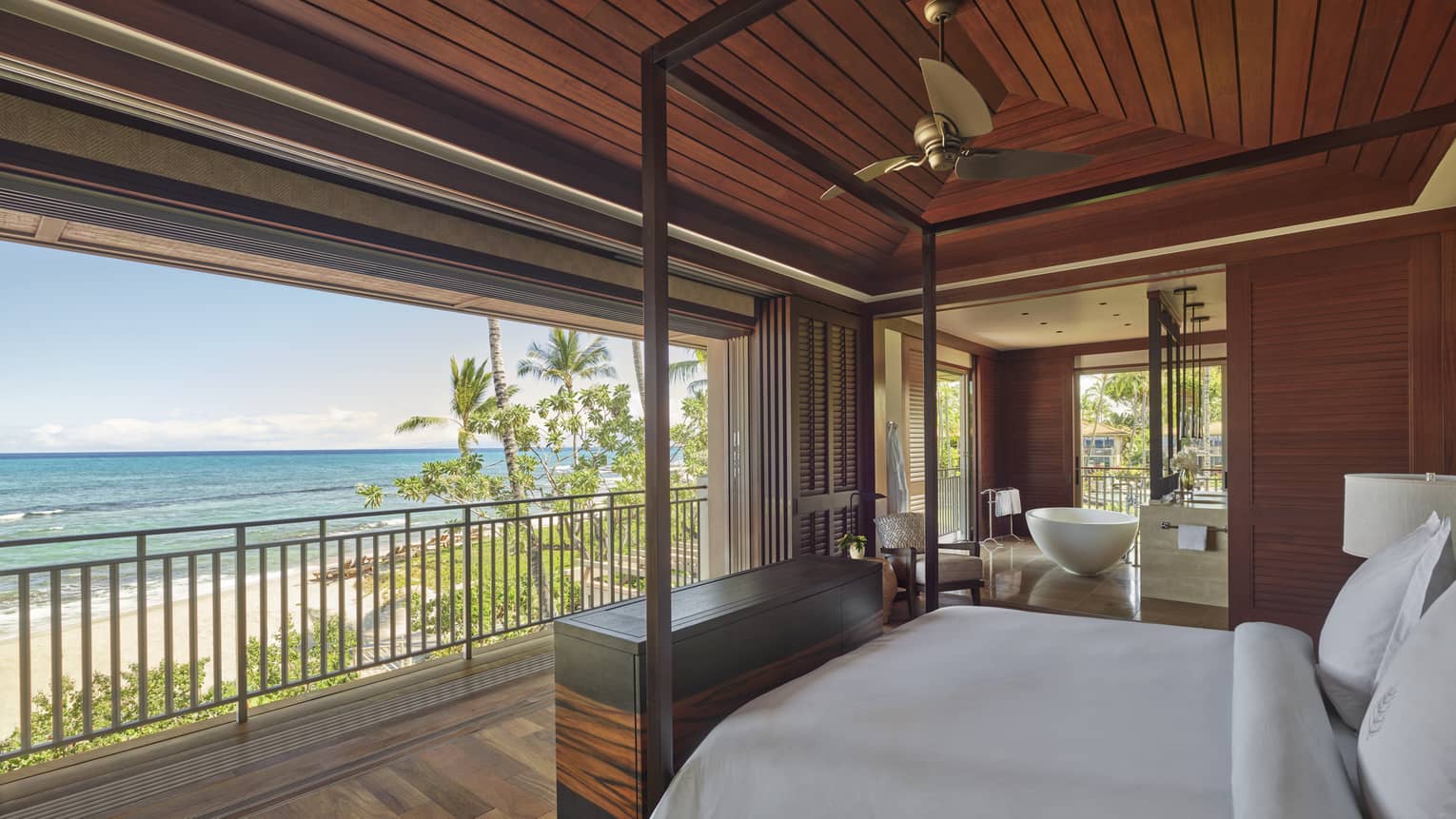 Bedroom with white king bed facing open wall, which looks out to tropical beach