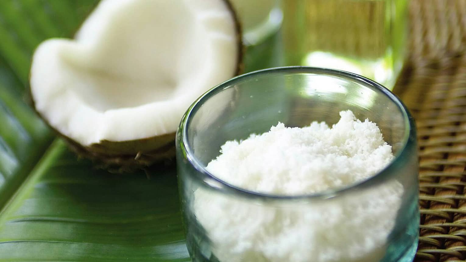 Half of a cracked coconut shell next to small glass bowl with coconut flakes