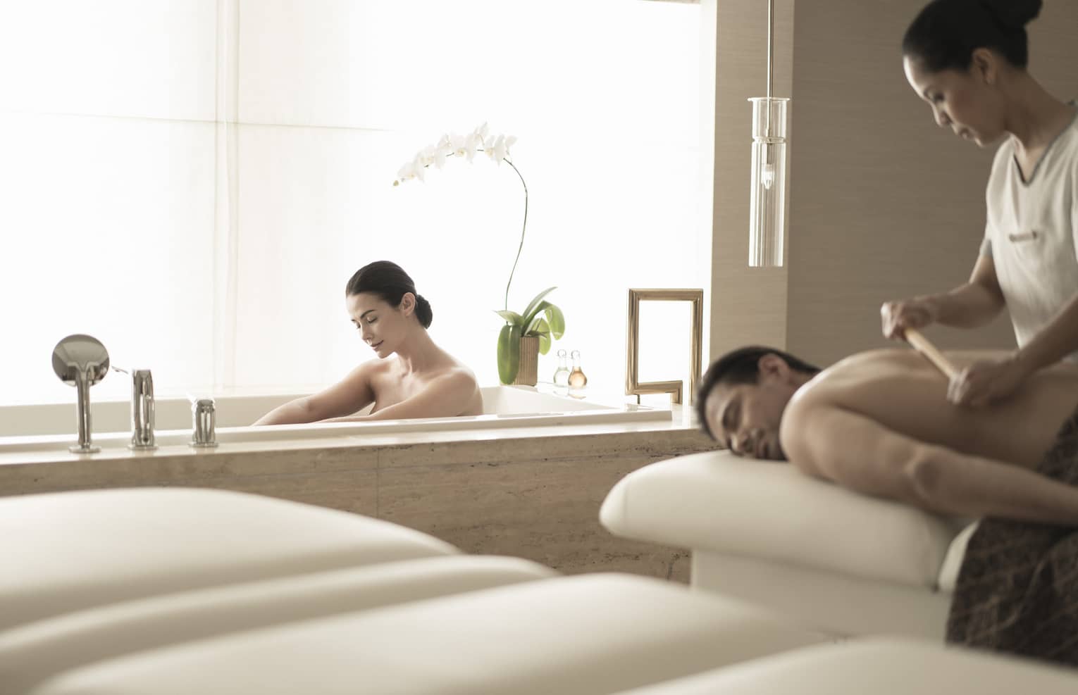 Woman soaks in spa tub near man getting massage