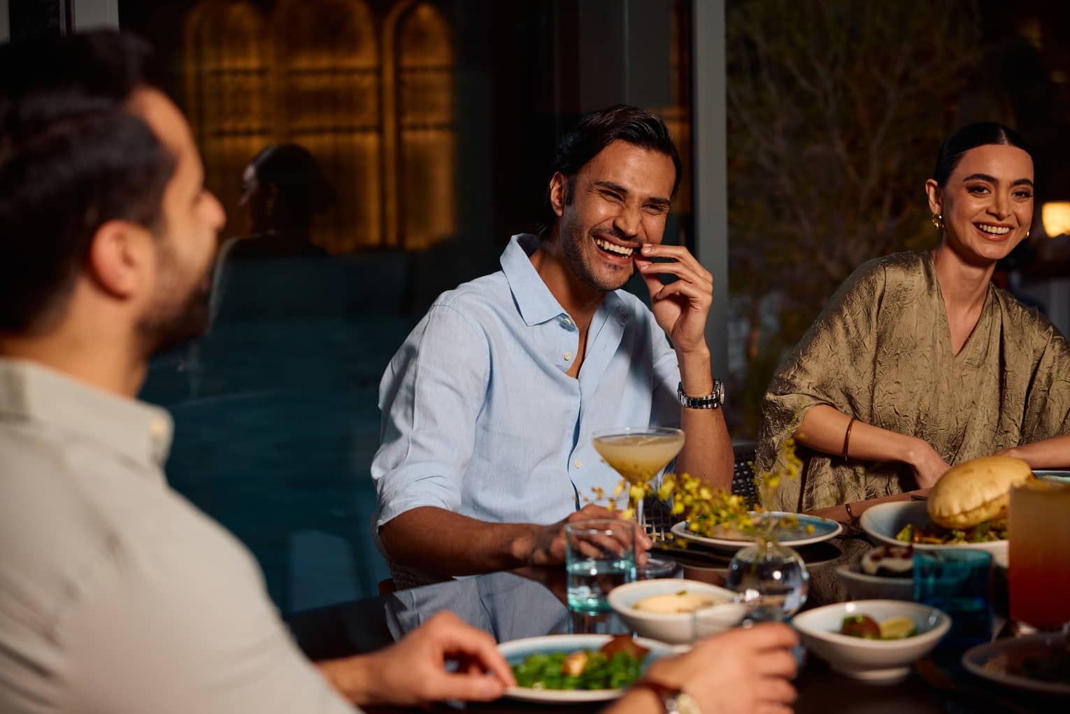 Three people sit smiling around a dining table
