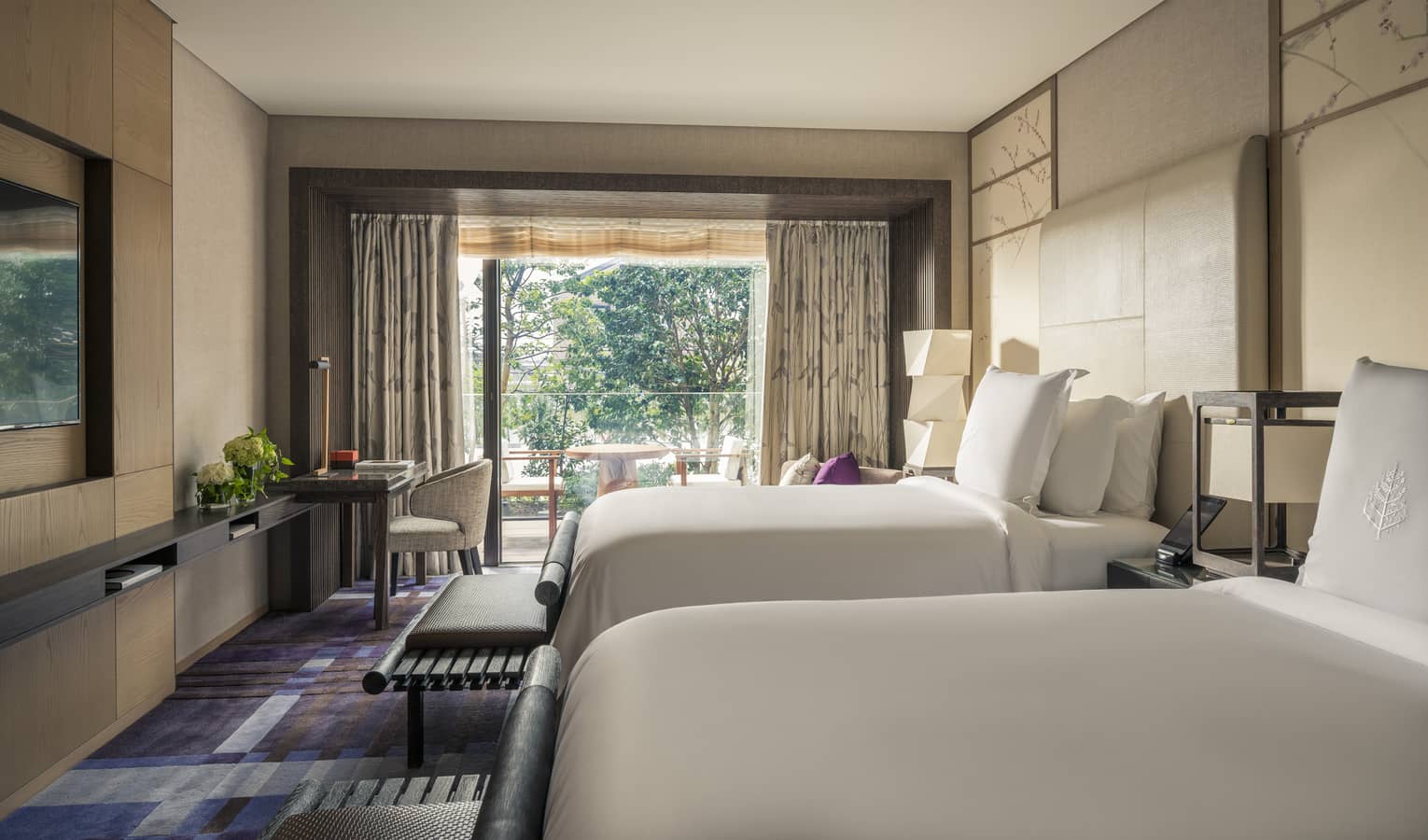 Hotel room with two beds, a work desk and a private balcony with outdoor seating and garden view