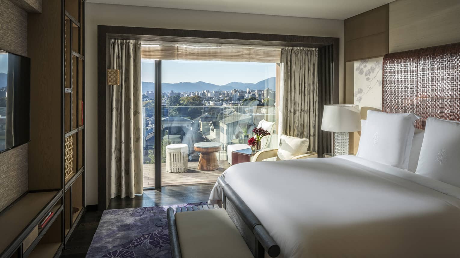 Luxury bedroom with a king bed, TV and sliding glass doors leading to a private balcony with scenic city and mountain views