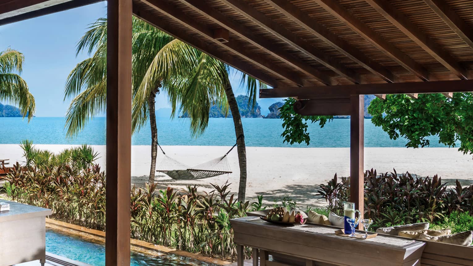 Villa awning over console table with fruit, drinks, plunge pool, by beach