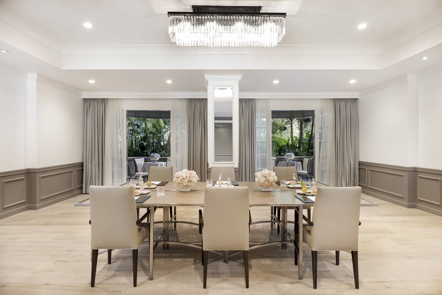 A large table with six chairs in a large room with beige accents and large windows.