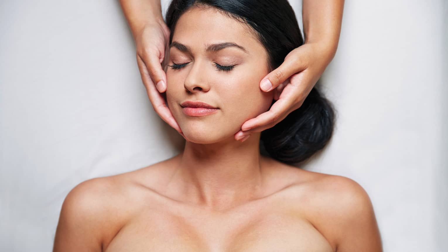 Woman with eyes closed as hands massage her face