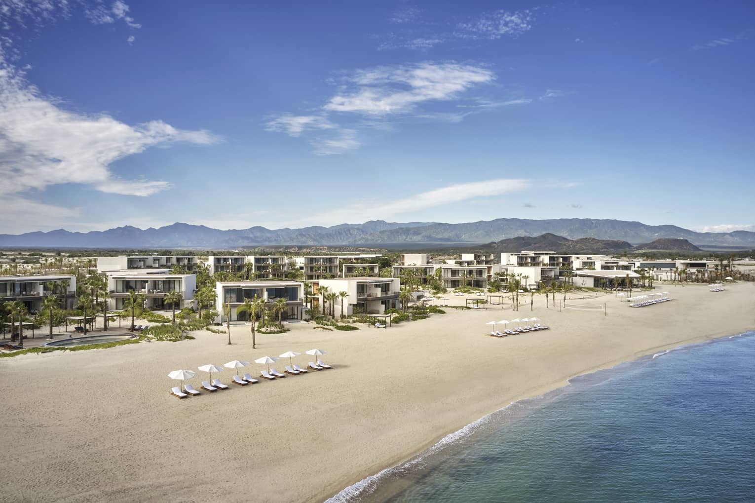 A beach with building and lounge chairs.