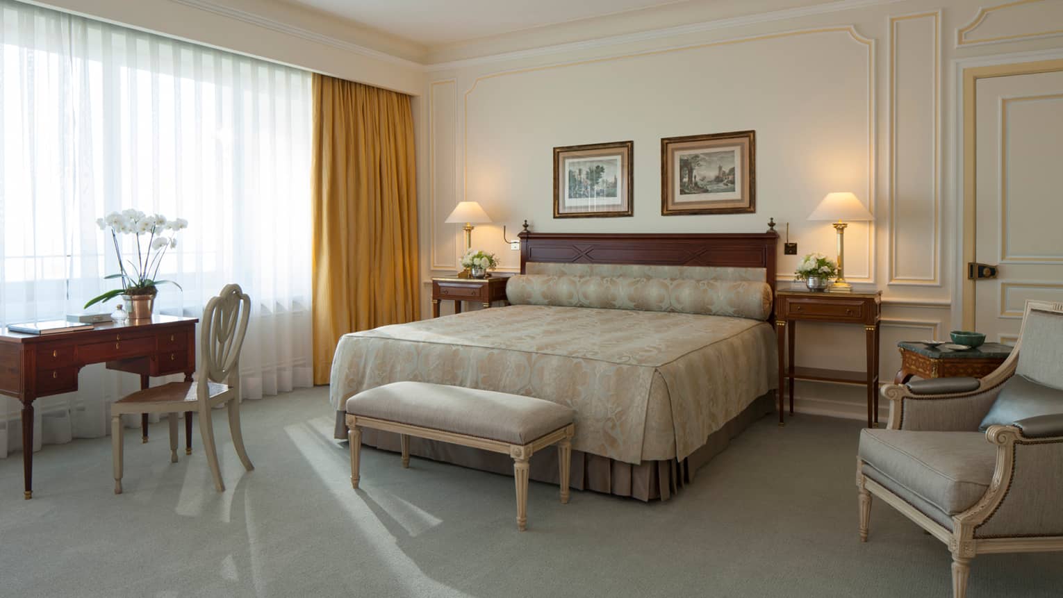 Royal Suite bed with gold pattern linens, light velvet bench and armchair, desk, sunny window with closed curtains