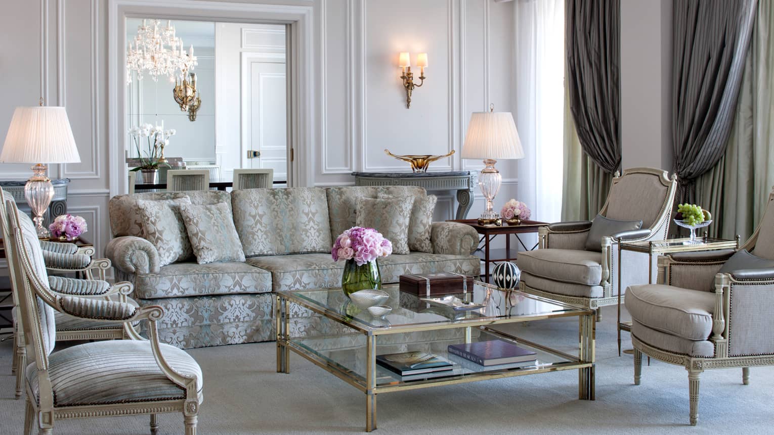 Royal Suite bright, elegant living room with blue-and-grey satin sofa, armchairs, glass coffee table with gold trim, white walls