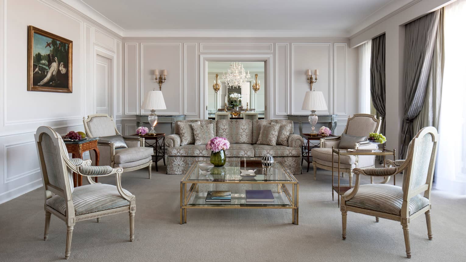 Sunny Royal Suite living room with blue-and-grey satin sofa with floral pattern, grey armchairs, glass coffee table with gold trim