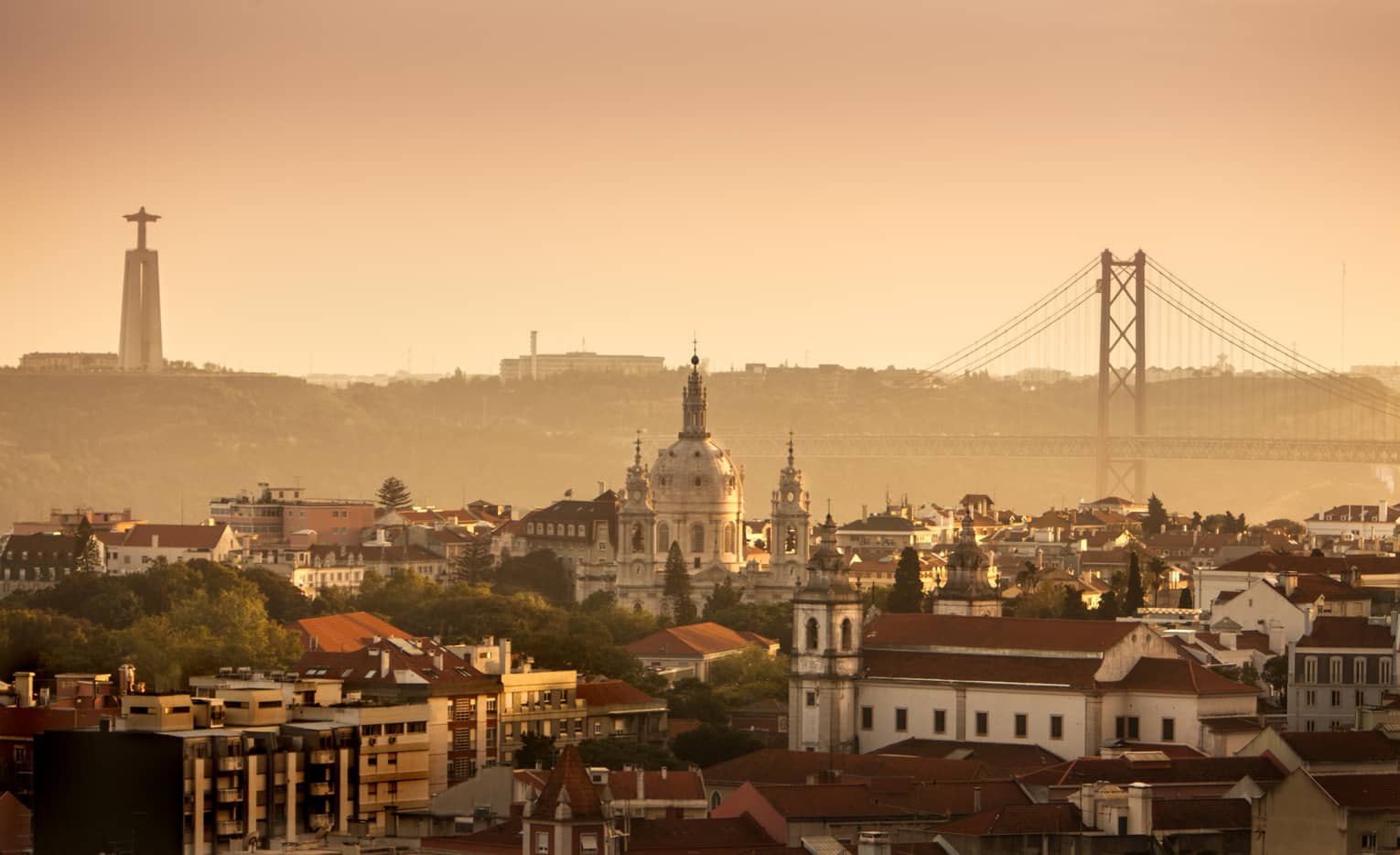 Orange haze over Lisbon buildings, skyline and bridge at sunset