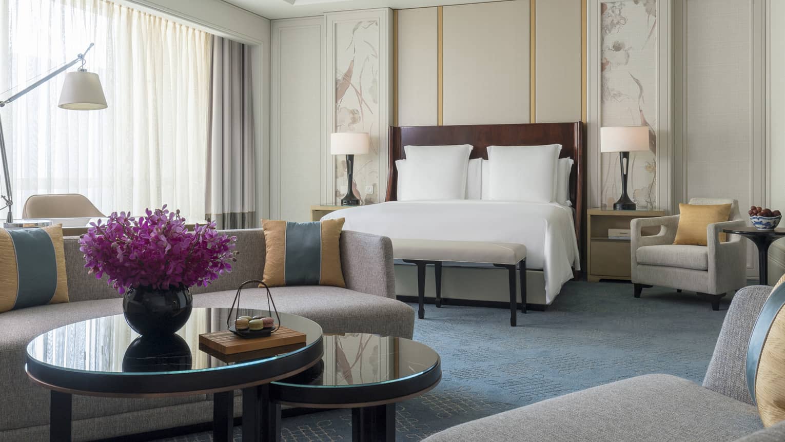 Junior Suite bed in front of grey sofa, coffee table with vase, purple flowers