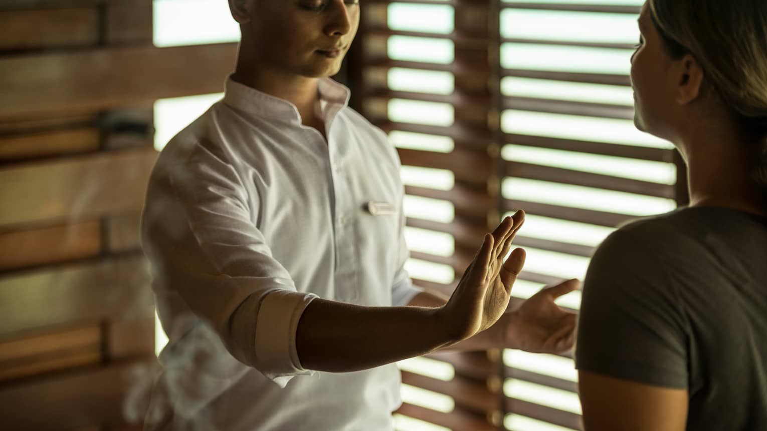 Reiki healer with eyes closed holds hand over woman's body