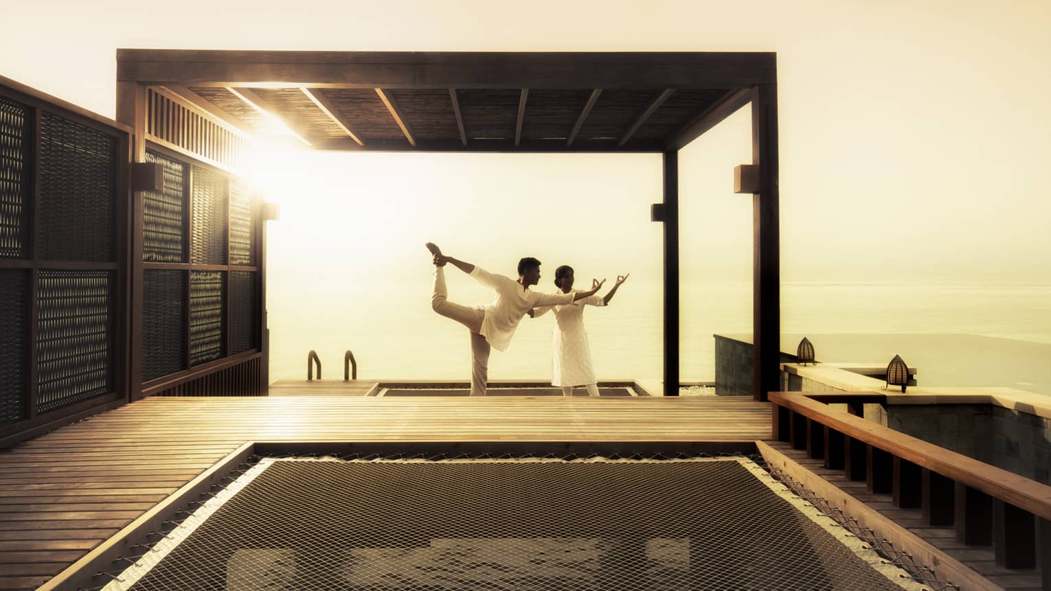 Yogi helps man stretch leg in yoga pose on patio near pool