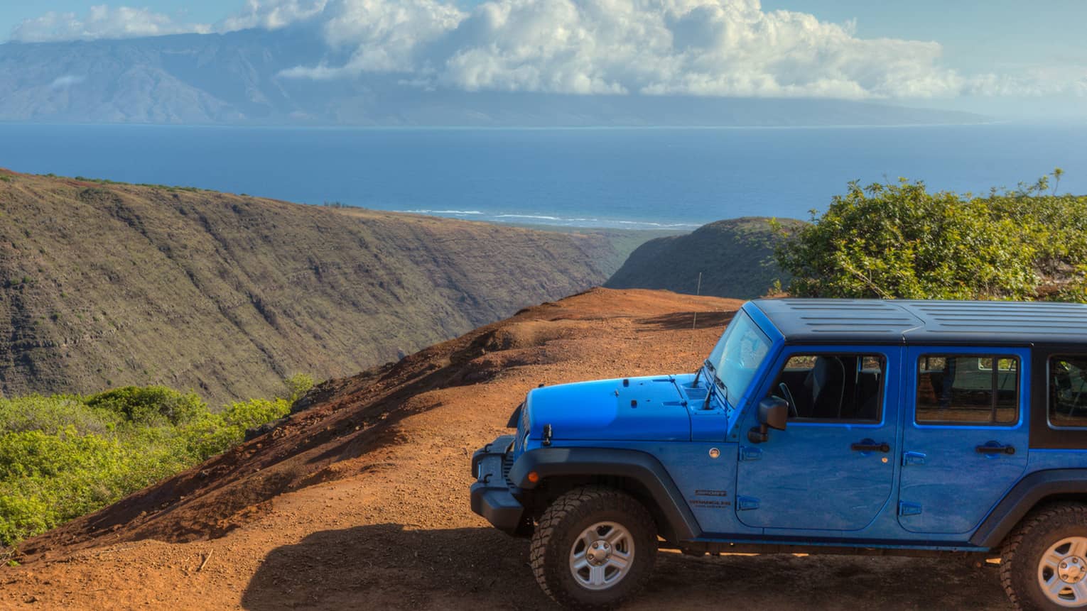 Blue four by four Jeep parked on dirt road overlooking canyon, hills