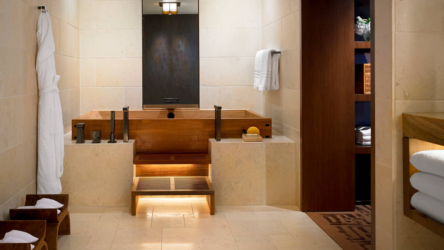White bathrobe hanging in Master bedroom bathroom with wood Japanese soaking tub, marble ledge, tile walls