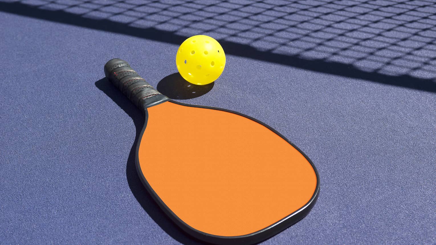 Orange pickleball paddle and yellow ball on blue table by net