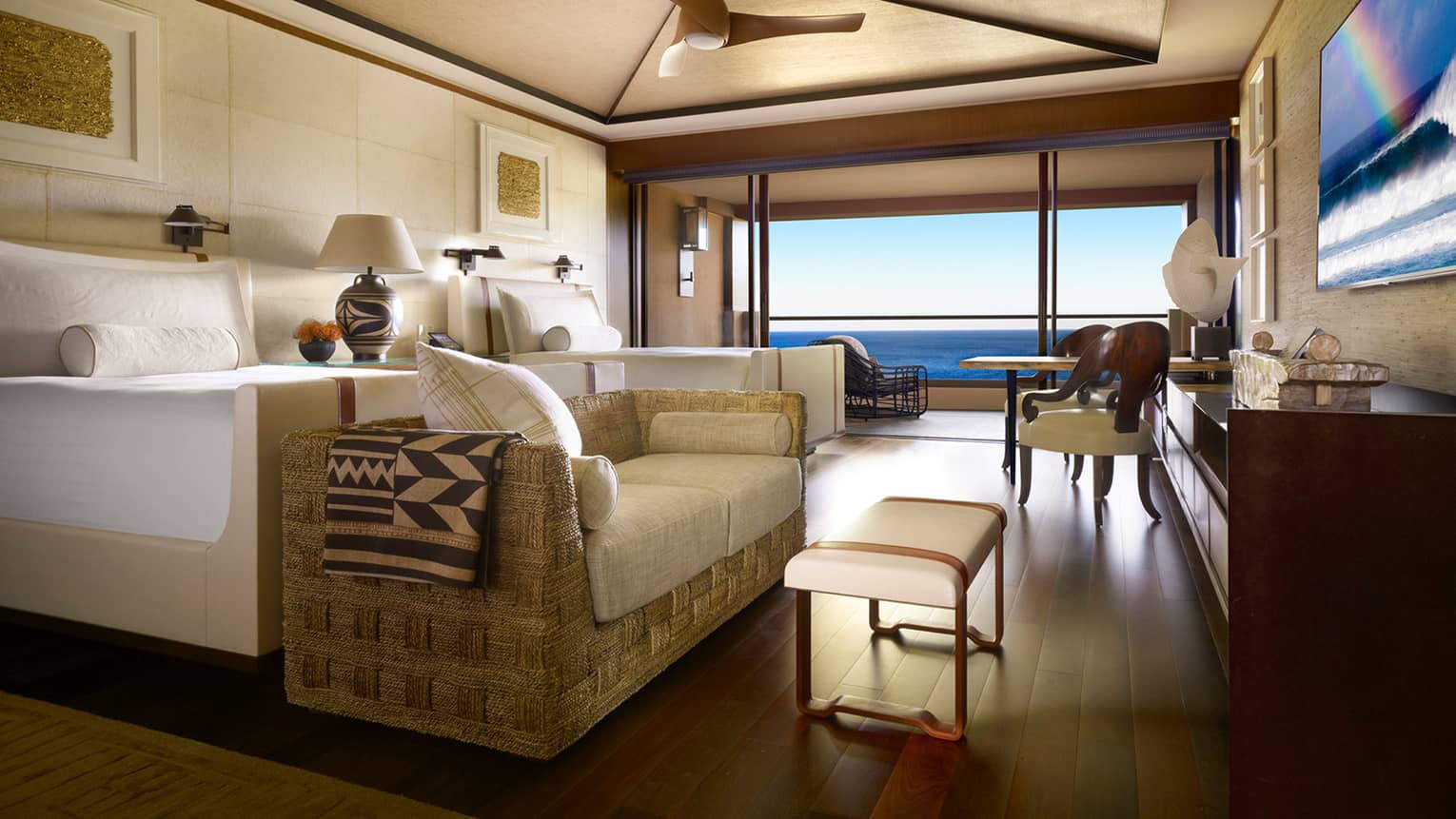 Close-up of rattan sofa with white cushions at foot of white bed near second bed by open patio door, ocean view