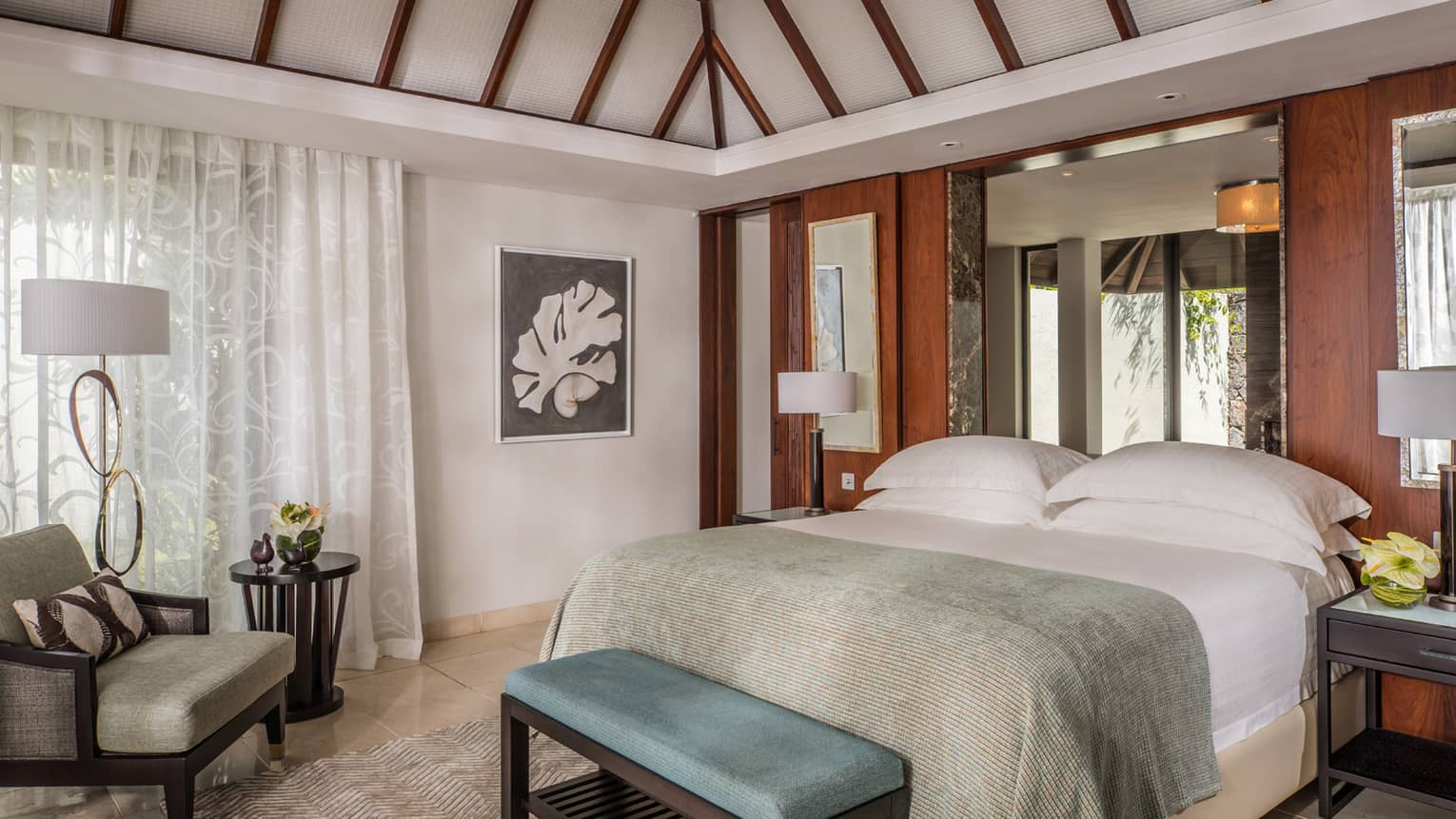 Residence Villa bed with light blue blanket, bench, armchair by drawn sheer white curtains