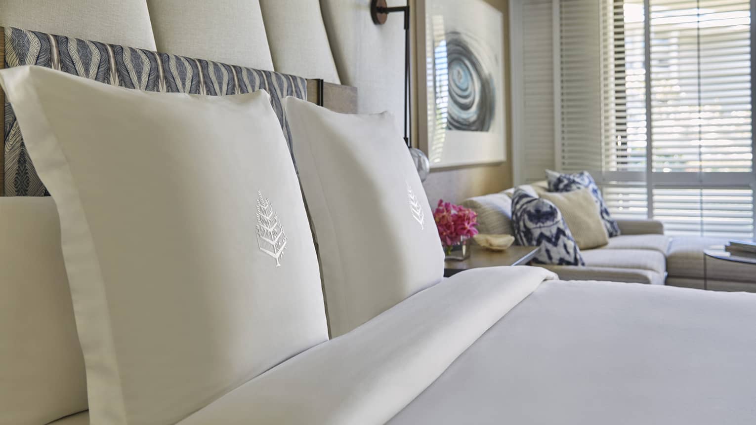 Close-up of a Four Seasons bed with white embroidered pillows, sofa with patterned pillows and wall art in the background