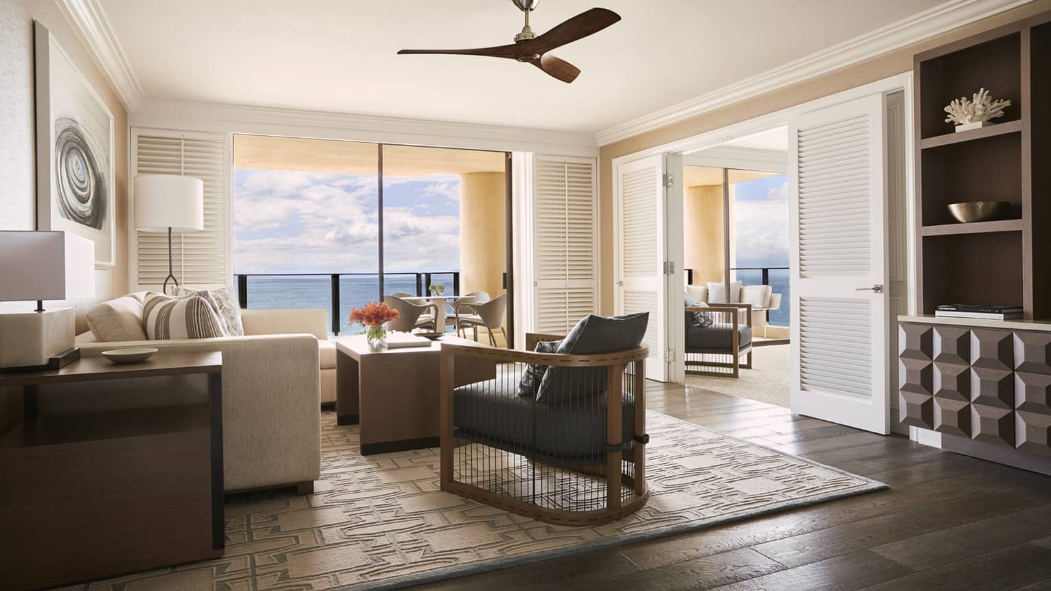 Bright living room with white sofa, wood armchair and ceiling fan, large windows with ocean view
