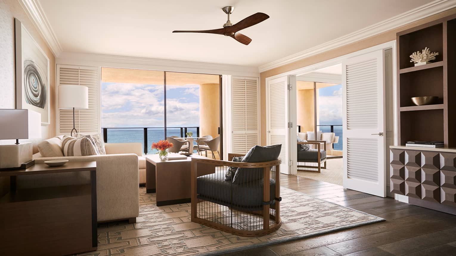 Luxury resort suite living area with ocean view, modern furniture, neutral decor and sliding doors leading to a balcony