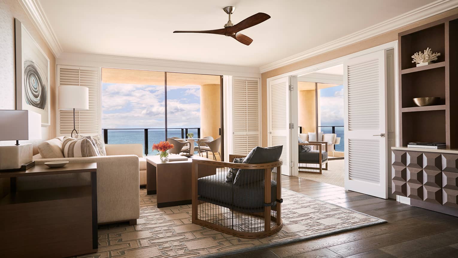 Bright living room with white sofa, wood armchair and ceiling fan, large windows with ocean view