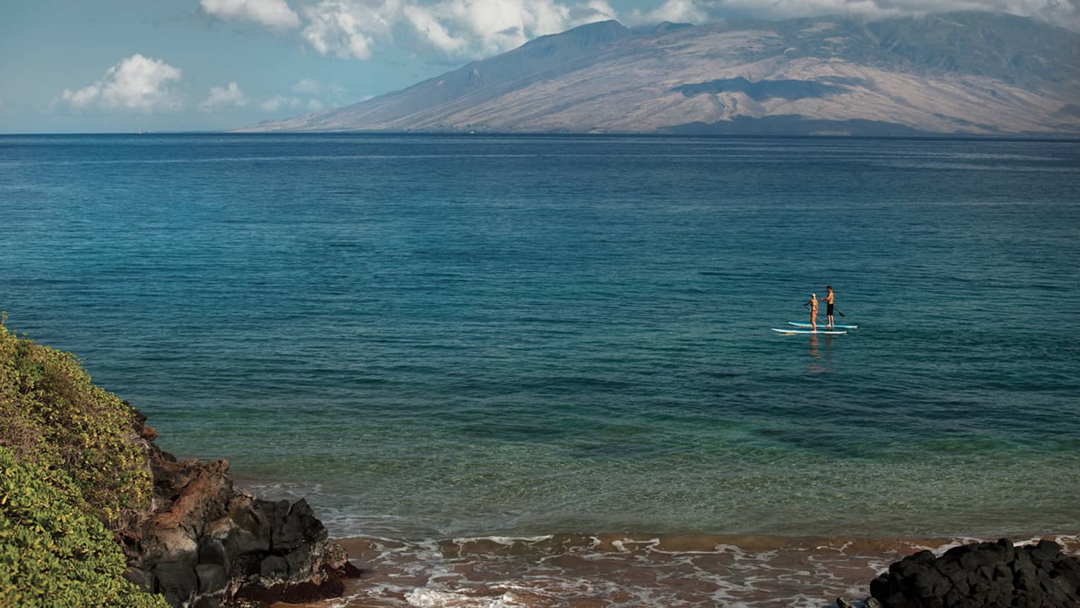 View from shore looking out at man and woman on stand-up paddleboards on ocean
