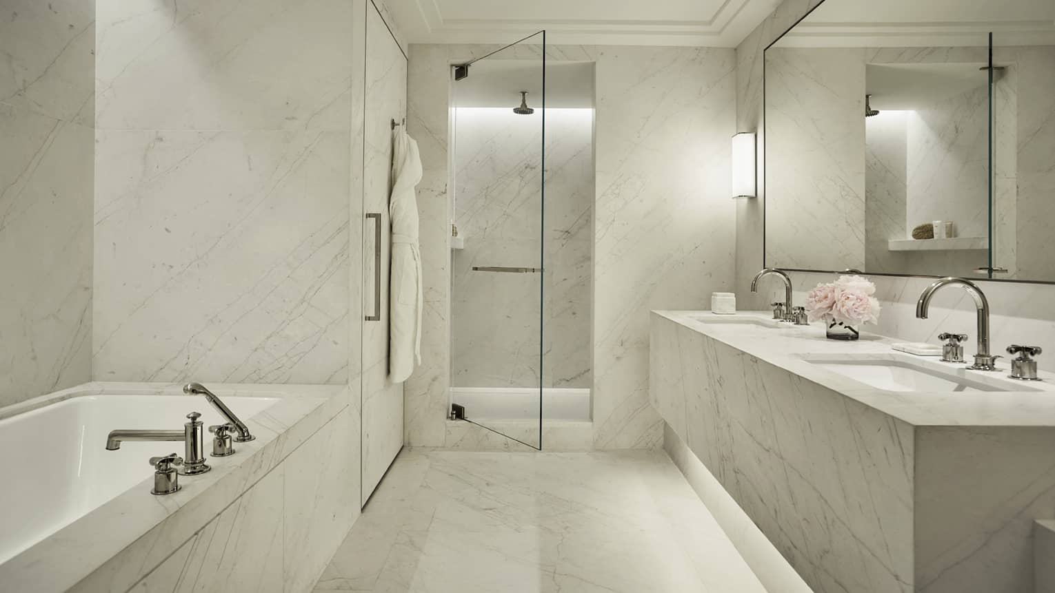 Luxury hotel bathroom with a marble bathtub, double sink vanity, walk-in shower with a glass door and elegant lighting