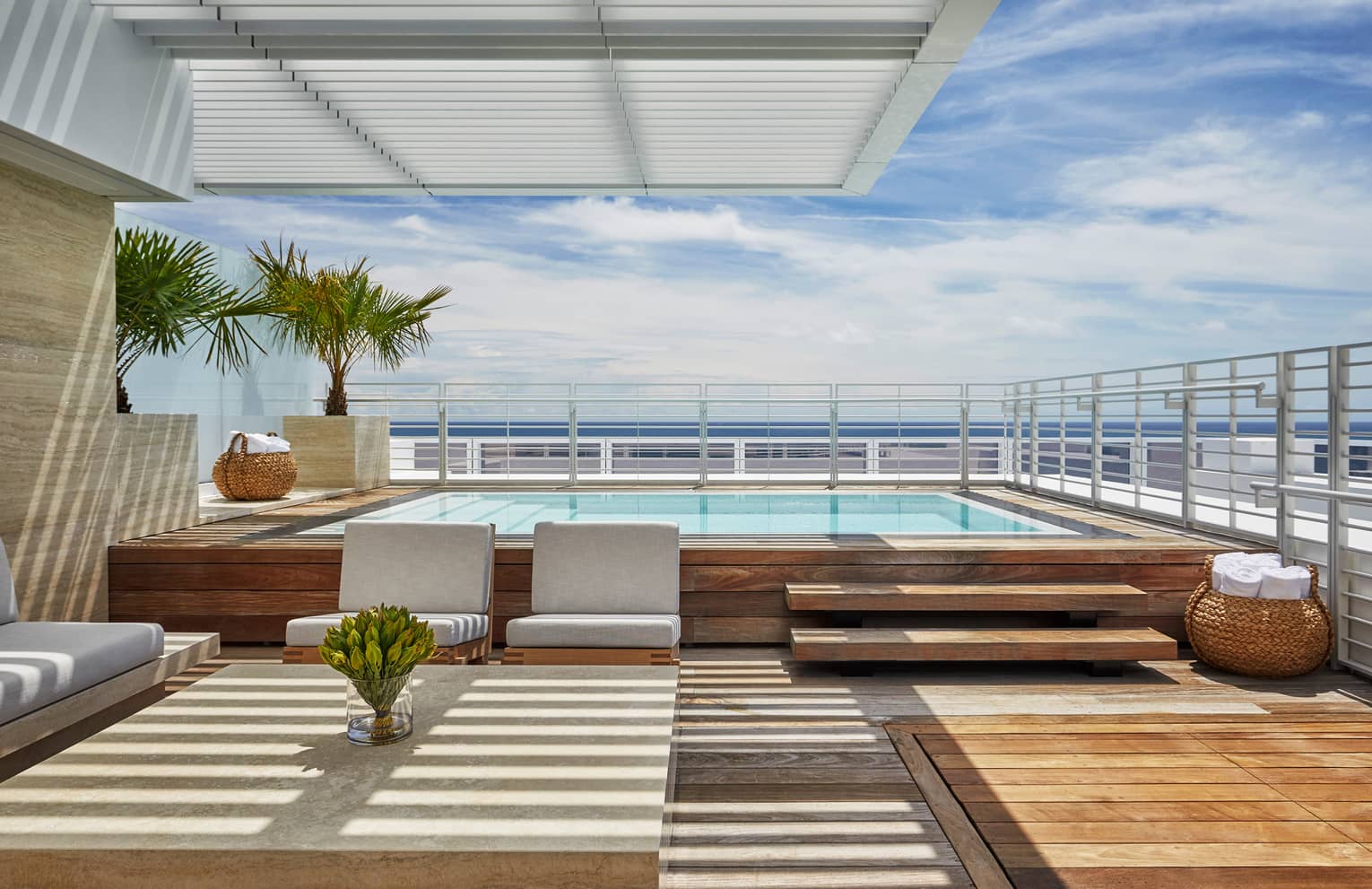 Luxury oceanfront penthouse terrace with a private pool, modern seating area, wooden deck and views of the ocean under a clear blue sky