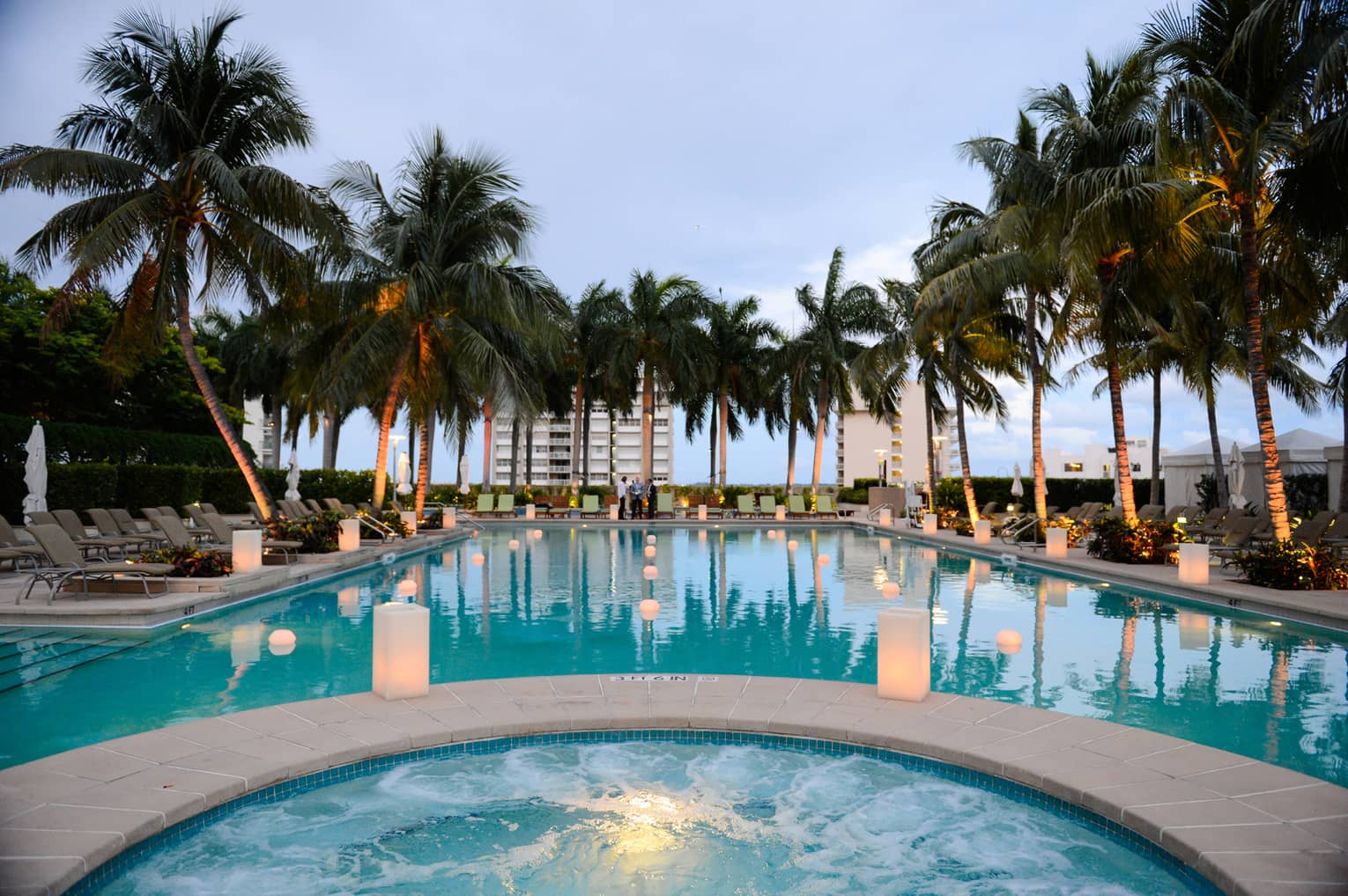 White lanterns glow along outdoor pool lined with palm trees