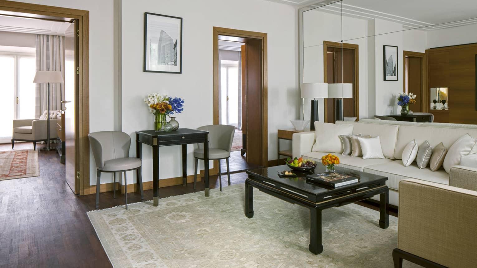 Hotel suite with white sofa and pillows against mirrored wall and flanked by chairs
