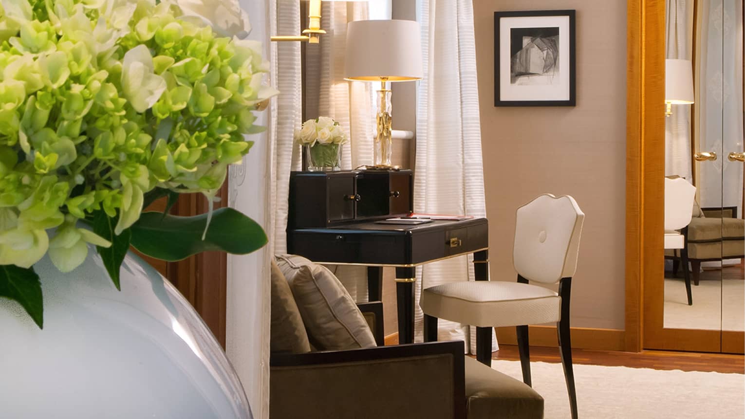 Hotel suite black secretary desk with white upholstered chair between windows  