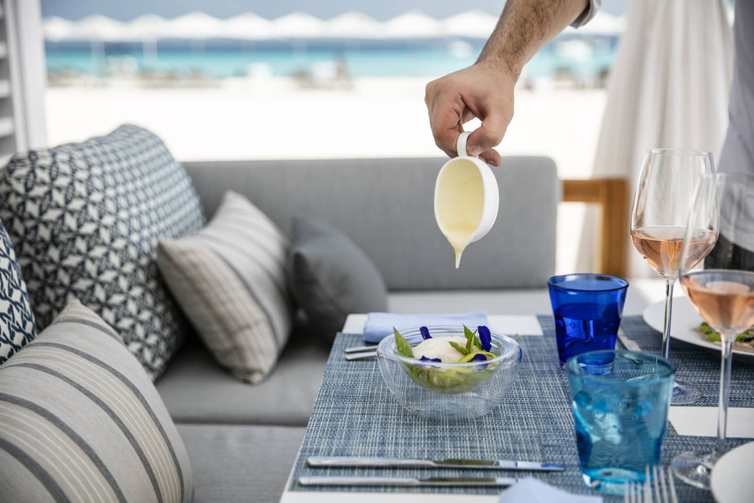 A person pouring some kind of glaze over a dish on a tastefully set table overlooking the ocean in Four Seasons Maldives - Landaa