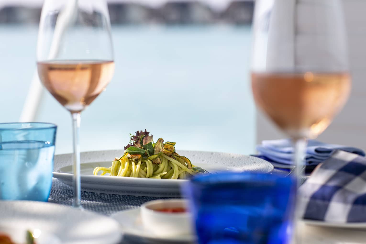A side view of a table with glasses of rose and a pasta dish over looking the ocean in Four Seasons Maldives - Landaa