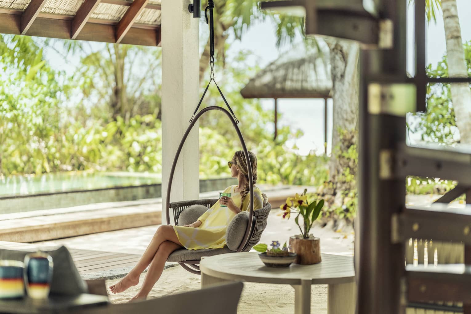 Woman in hanging bucket chair sits poolside in Beach Villa