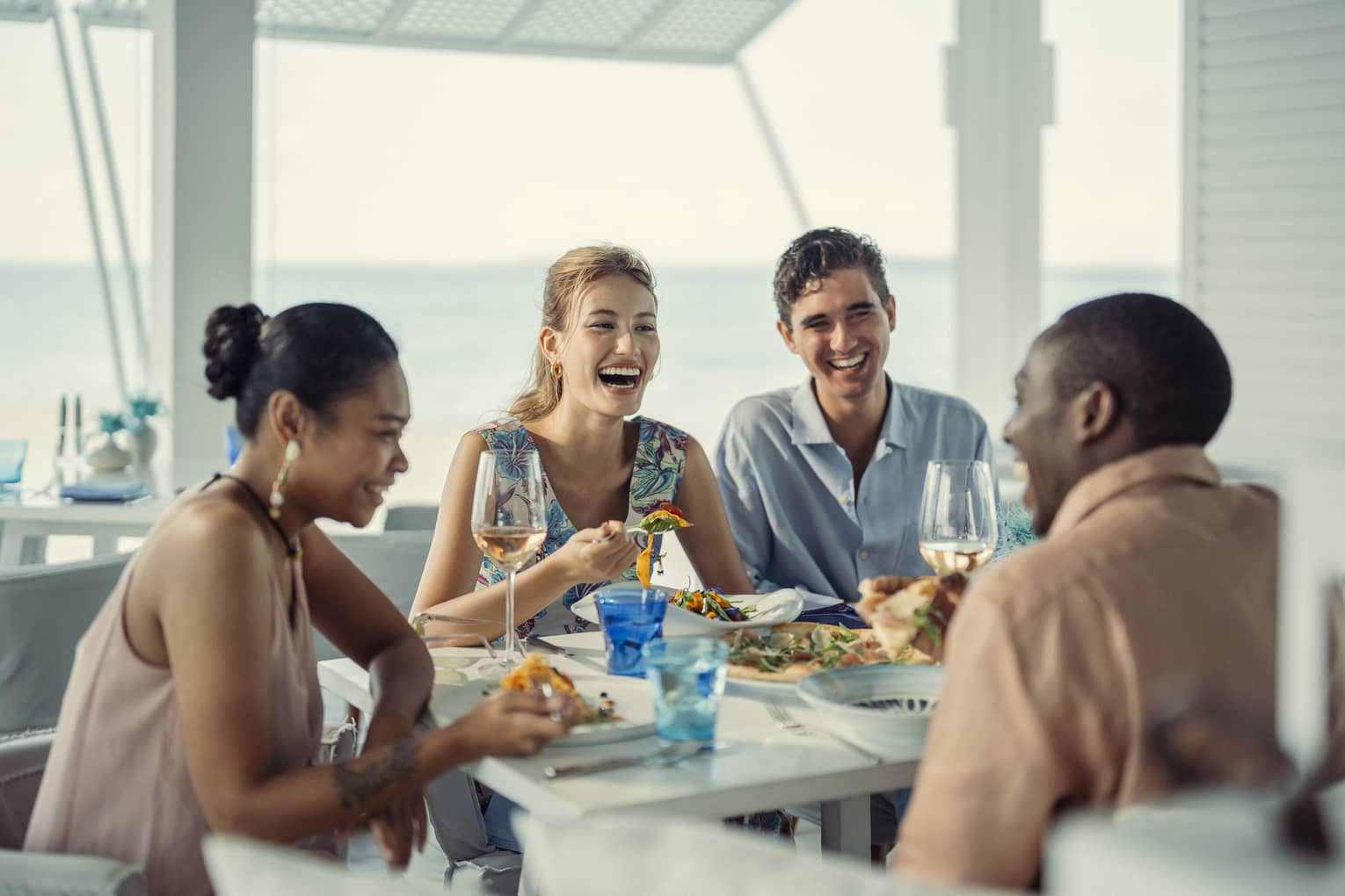 Two couples laugh over a meal at Blu Beach Club