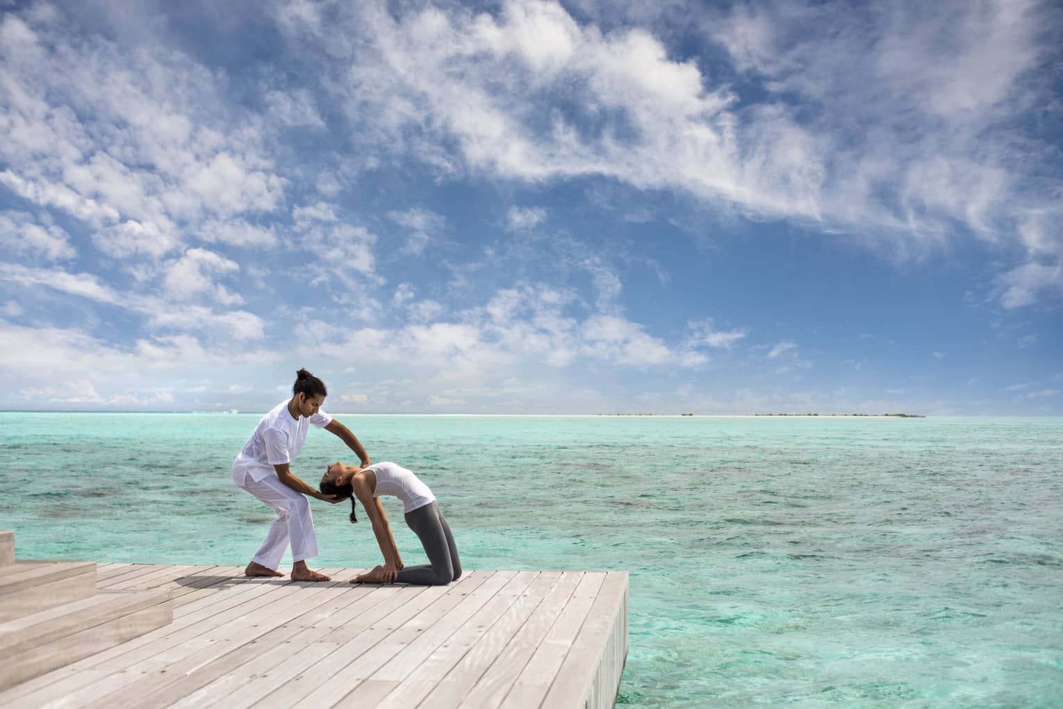 Woman leans back into hands of Yoga Therapist on dock over lagoon