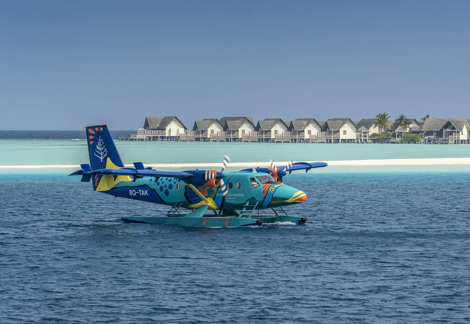 The Four Seasons sea plane landing on calm water in front of beach houses and palm trees