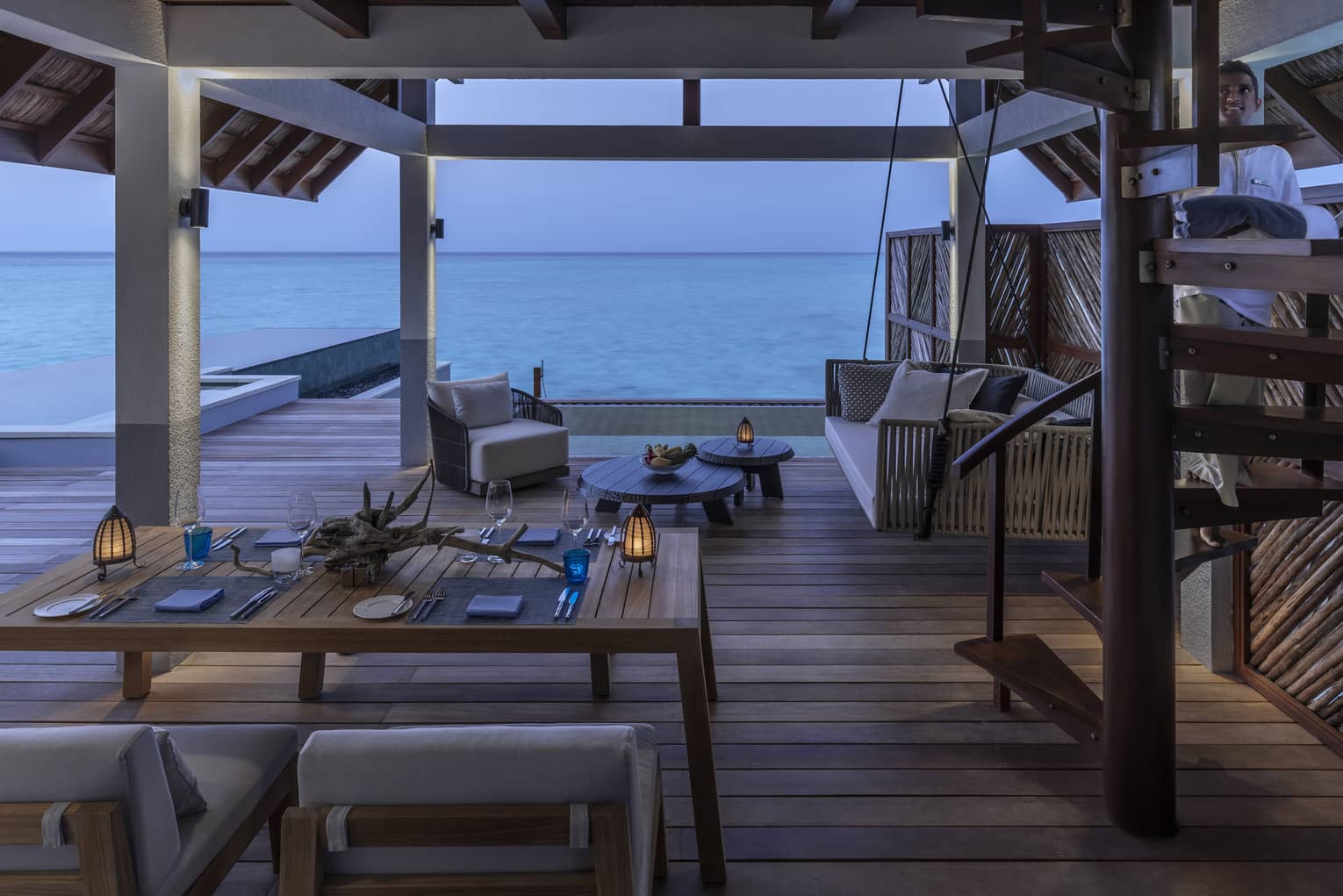 A dining table is arranged near the lounge area of an Over Water Villa with an ocean view