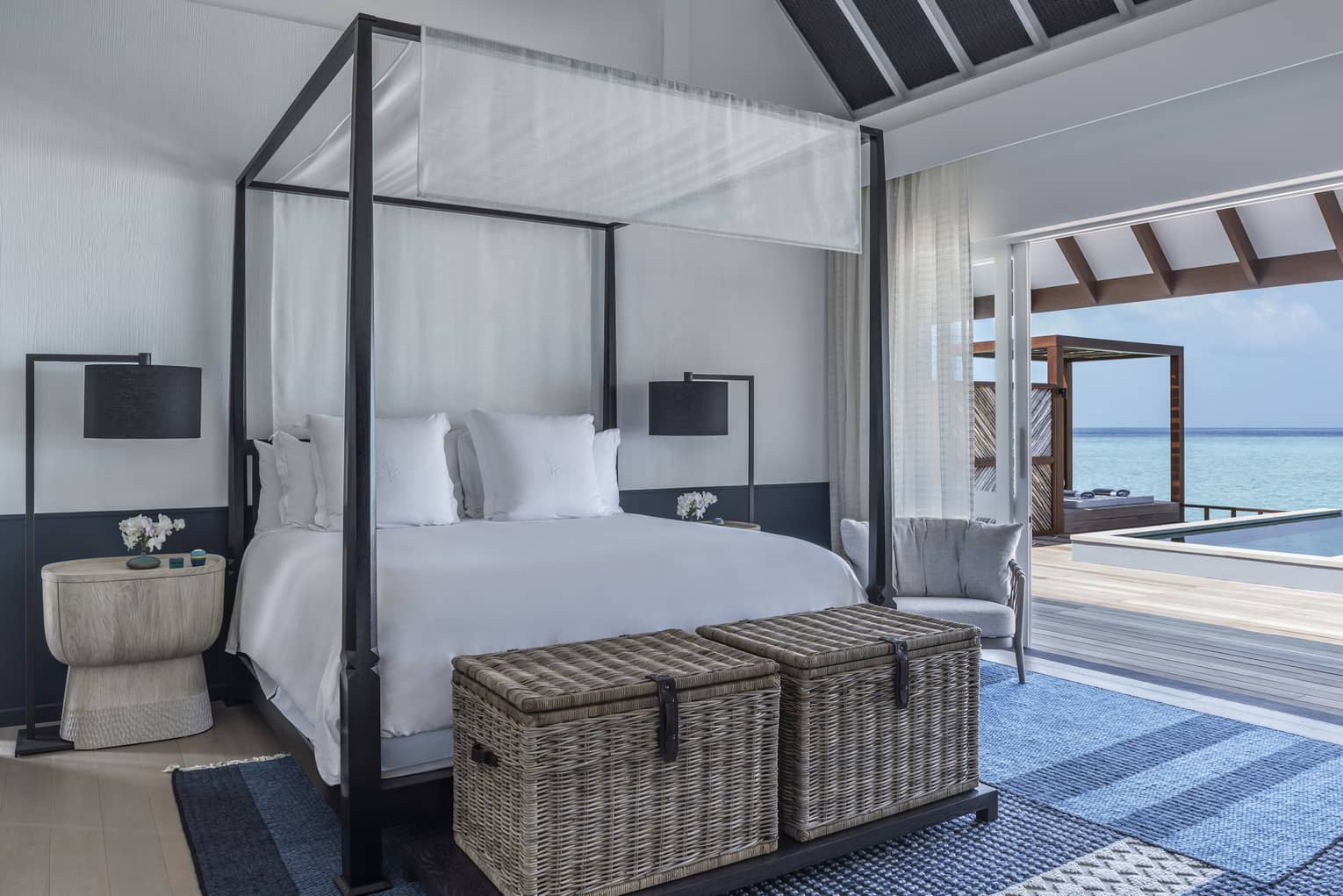 A four poster bed near a sliding door leading to an oceanside pool