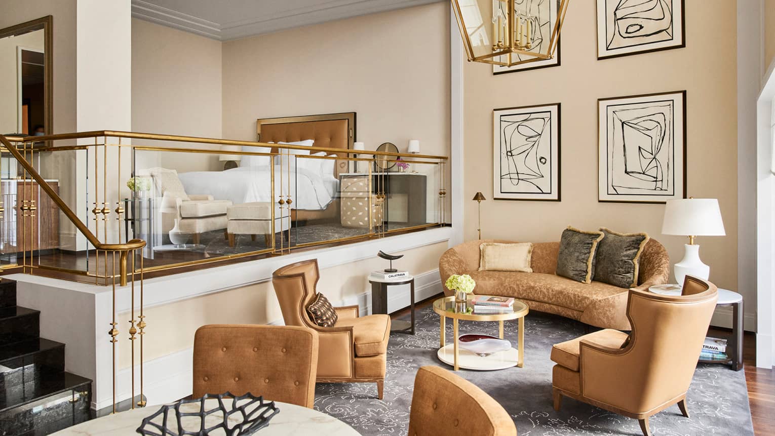 Luxury hotel loft suite with a raised king bed, armchair with ottoman, gold railing, sitting area with plush sofa, armchairs, coffee table and abstract wall art