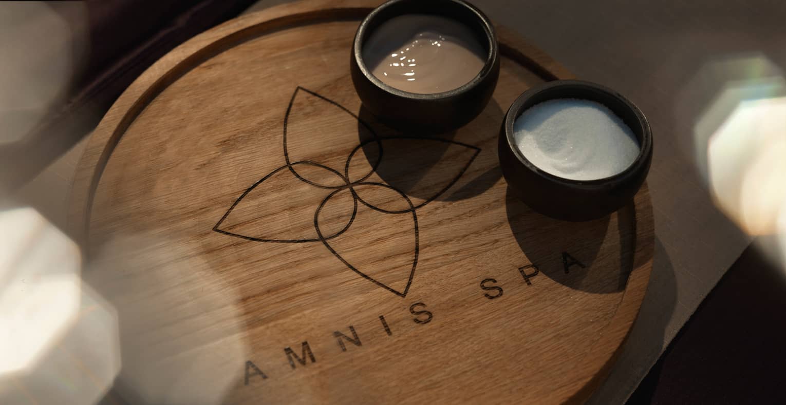 Wood tray with Amnis Spa logo and two small black bowls with cream and salt