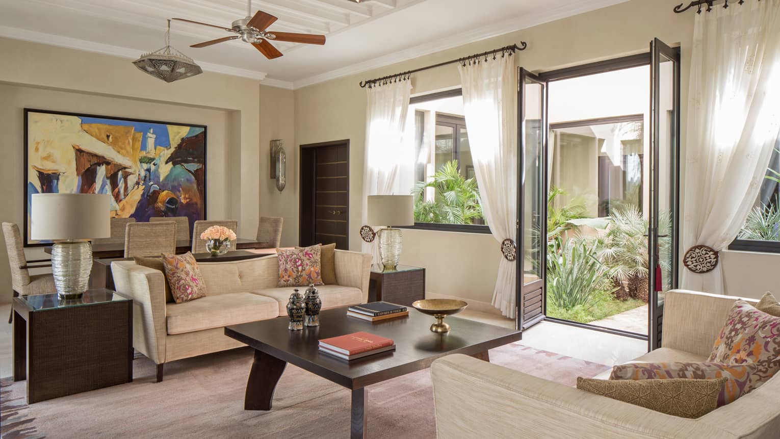 Two Bedroom Villa living room with two sofas around large coffee table with books, dining table, large colourful painting