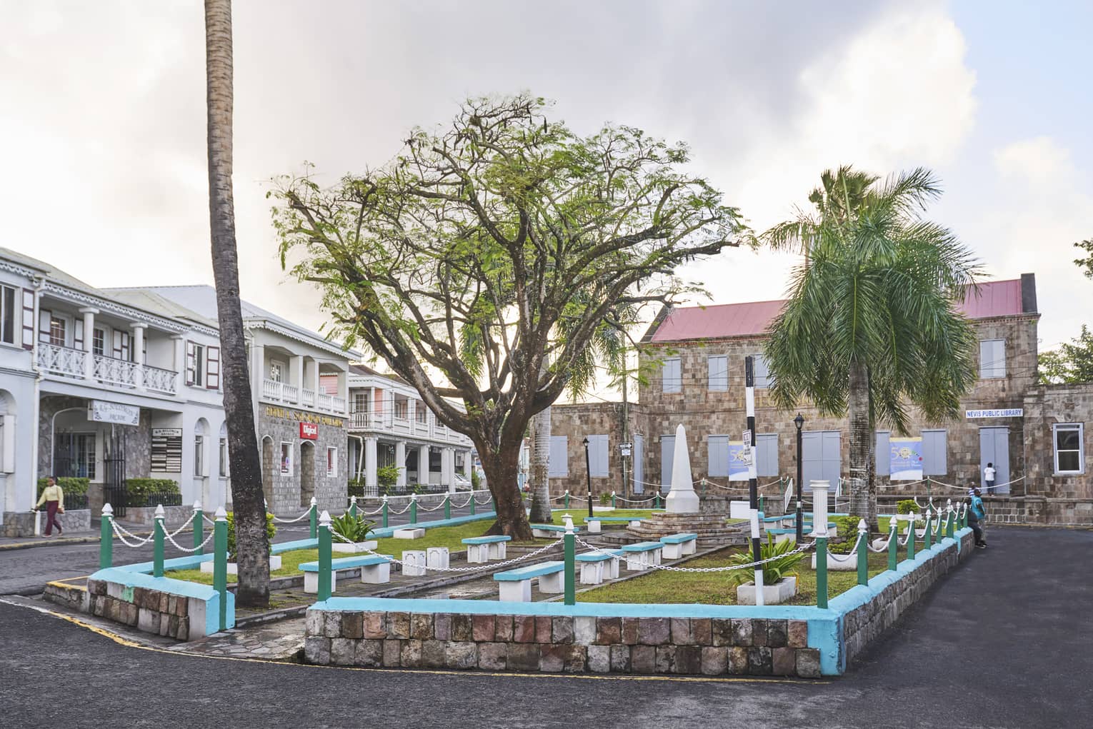 A small outdoor sitting area on a street with benches, grass and trees.